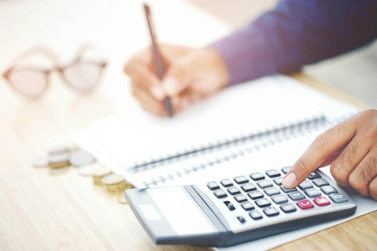 Man Using Calculator and Writing on Notebook on Table